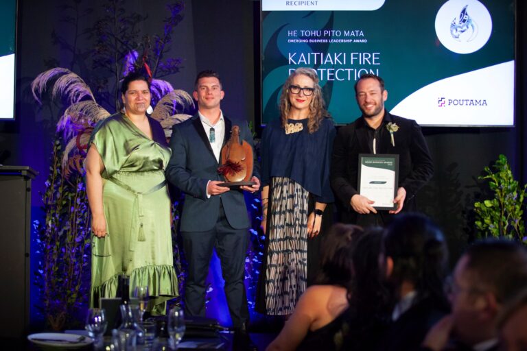 A man accepting an award on stage with two women and another man at the Kuma Awards.